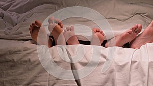 Family legs dancing under blanket on the sheet in the evening. Happy father, mother and kid child boy son with bare feet