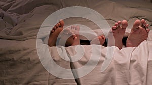 Family legs move toes on sheet under the blanket falling asleep in evening. Happy man father, woman mother and child kid