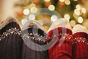 family legs in stylish festive socks on background of golden beautiful christmas tree with lights in festive room. relax time tog