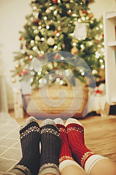 family legs in stylish festive socks on background of golden beautiful christmas tree with lights in festive room. relax time tog