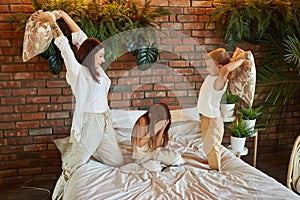 Family leisure. Mom son and daughter fight on pillows on the bed in the bedroom. Joy and fun.