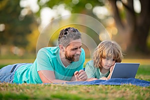 Family, leisure and people concept. Happy father and son with tablet pc computer laying on grass. Kid with daddy