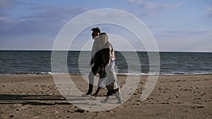 Family, leisure and people concept - happy mother, father and little son walking along autumn beach. Side view. Slow