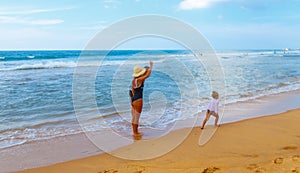 Family with little dother holding hands and walking on sand tropical beach waves and people in the background photo