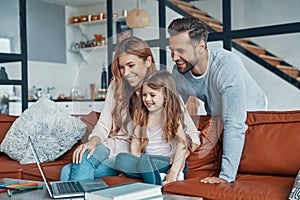 Family with little girl bonding together and smiling while using laptop at home