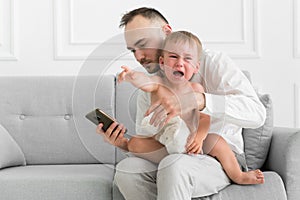 Family in the living room father and little child crying while man is busy with the phone - social problem