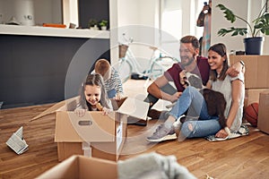 Family in living room have a fun spend time at new home. playful laughing girl sitting at cardboard box, boy rolling her playing