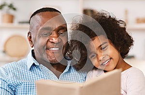 Family lockdown hobbies. African American child listening to her grandfather read bedtime story at home photo