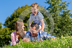 Family lying in grass on meadow, son riding on dad