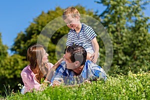 Family lying in grass on meadow, son riding on dad