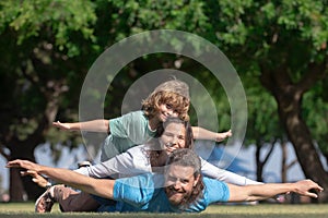Family lying on grass in park. Parents giving child piggybacks in countryside. Fly concept, little boy is sitting