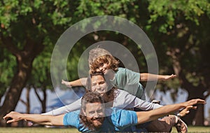 Family lying on grass in park. Parents giving child piggybacks in countryside. Fly concept, little boy is sitting