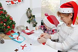 Family making seasonal greeting cards together at christmas time, grandmother with granddaughter at home