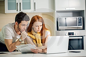 Family managing budget, reviewing their bank accounts using laptop in kitchen