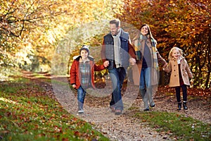 Family With Mature Parents And Two Children Holding Hands Walking Along Track In Autumn Countryside