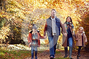 Family With Mature Parents And Two Children Holding Hands Walking Along Track In Autumn Countryside