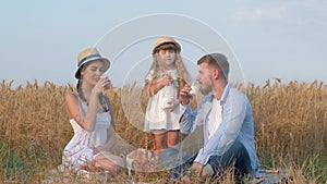Family meadow picnic, little child girl pours milk into her parents glasses and they communicate drinking milk while
