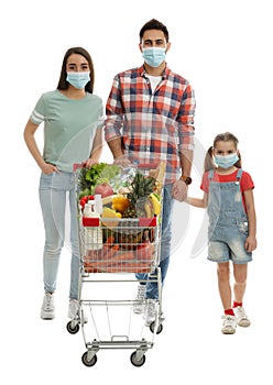Family in medical masks with shopping cart full of groceries on white background