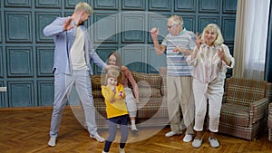 Family members of different generations having fun listening music, dancing crazy in room at home