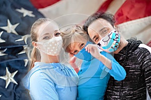 Family members embracing each other, smiling in the camera wearing cloth face masks with the US flag on the background