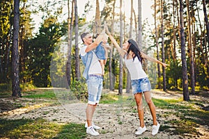 Family mom, dad and daughter sits at the daddy on the shoulders, and parents kiss on the nature in the forest in the summer at