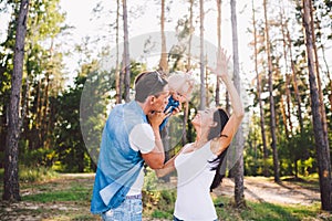 Family mom, dad and daughter sits at the daddy on the shoulders, and parents kiss on the nature in the forest in the summer at