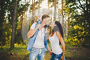 Family mom, dad and daughter sits at the daddy on the shoulders, and parents kiss on the nature in the forest in the summer at sun