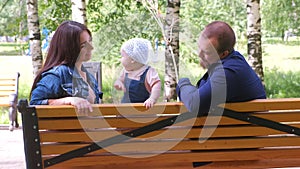 Family mom and dad sitting and playing on bench in city park with baby girl.