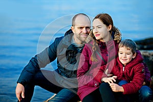Family mom, dad and son sitting on the beach by the sea. Season - spring, autumn. The concept of family happiness