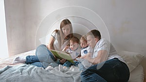 Family mom, dad and two twin brothers read books laying on the bed. Family reading time.