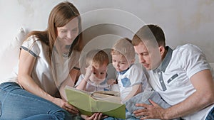 Family mom, dad and two twin brothers read books laying on the bed. Family reading time.
