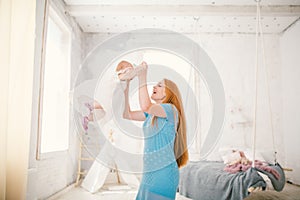 Family mom and daughter one year old entertain themselves inside the interior. The woman puts the child`s arms up and pushes her