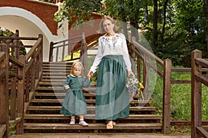 Family mom with daughter in vintage retro style linen dresses with bouquet walking dawn wooden stairs in a park garden