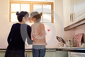 Family, mom and girl kiss in kitchen washing dishes for help, learning and development of house skills . Cleaning