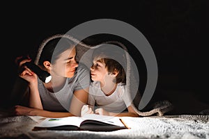 Family Mom and little son reading a book with a flashlight under the blanket