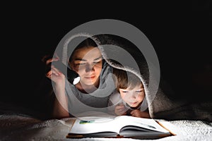 Family Mom and little son reading a book with a flashlight under the blanket