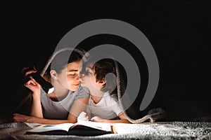 Family Mom and little son reading a book with a flashlight under the blanket