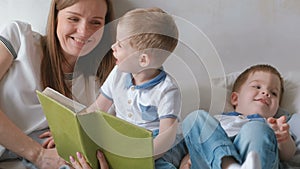 Family mom and two twin brothers toddlers read books laying on the bed. Family reading time.