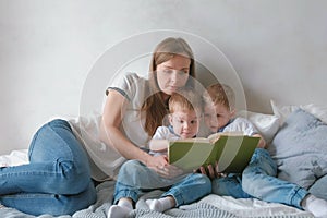 Family mom and two twin brothers toddlers read books laying on the bed. Family reading time.