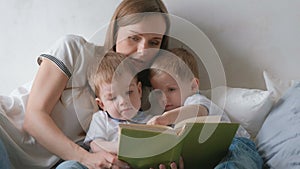 Family mom and two twin brothers toddlers read books laying on the bed. Family reading time.
