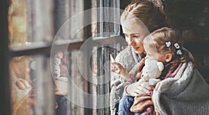 Family mother and child daughter look out window on rainy autumn