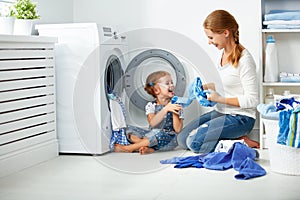 Family mother and child girl little helper in laundry room near washing machine