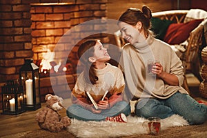 Family mother and child reading book and drink tea on winter evening by fireplace