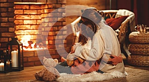 Family mother and child reading book and drink tea on winter evening by fireplace