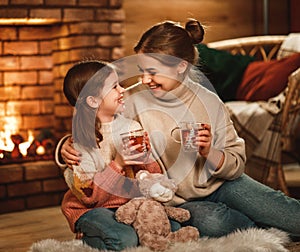 Family mother and child reading book and drink tea on winter evening by fireplace