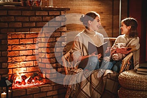 Family mother and child reading book and drink tea on winter evening by fireplace