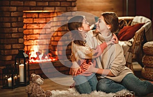 Family mother and child reading book and drink tea on winter evening by fireplace