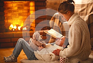 family mother and child reading book on winter evening by fireplace.