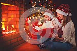 Family mother and children read a book at christmas near fire