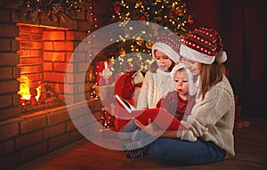 Family mother and children read a book at christmas near firep